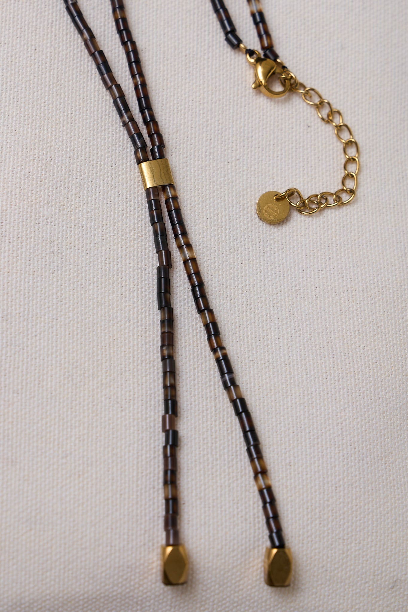 Stone lariat necklace - dark brown with small cylindrical beads and gold-tone clasp and accents for a subtle, earthy touch.