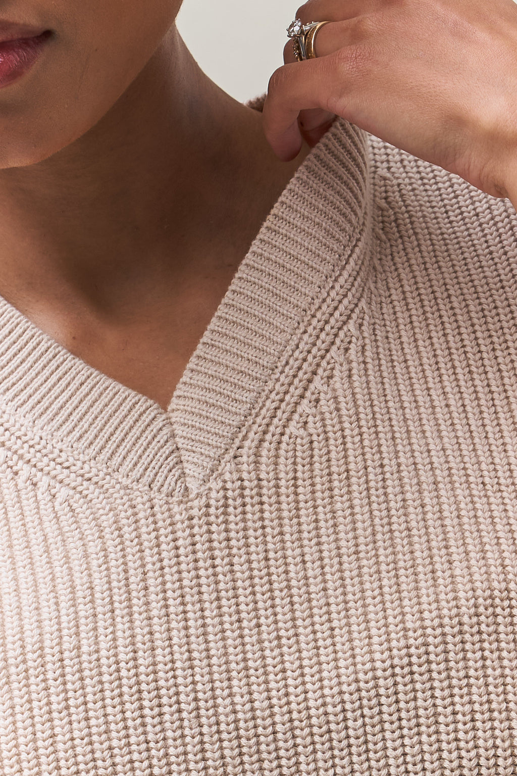 V-neck knit vest in soft beige cotton with a textured knit that holds its shape over time for relaxed layering.
